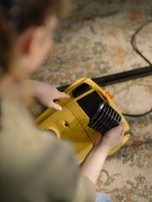 A person operating a yellow portable industrial fan or dehumidifier on a decorative area rug in a residential space during surface cleaning or deep cleaning. The object features adjustable vents and h